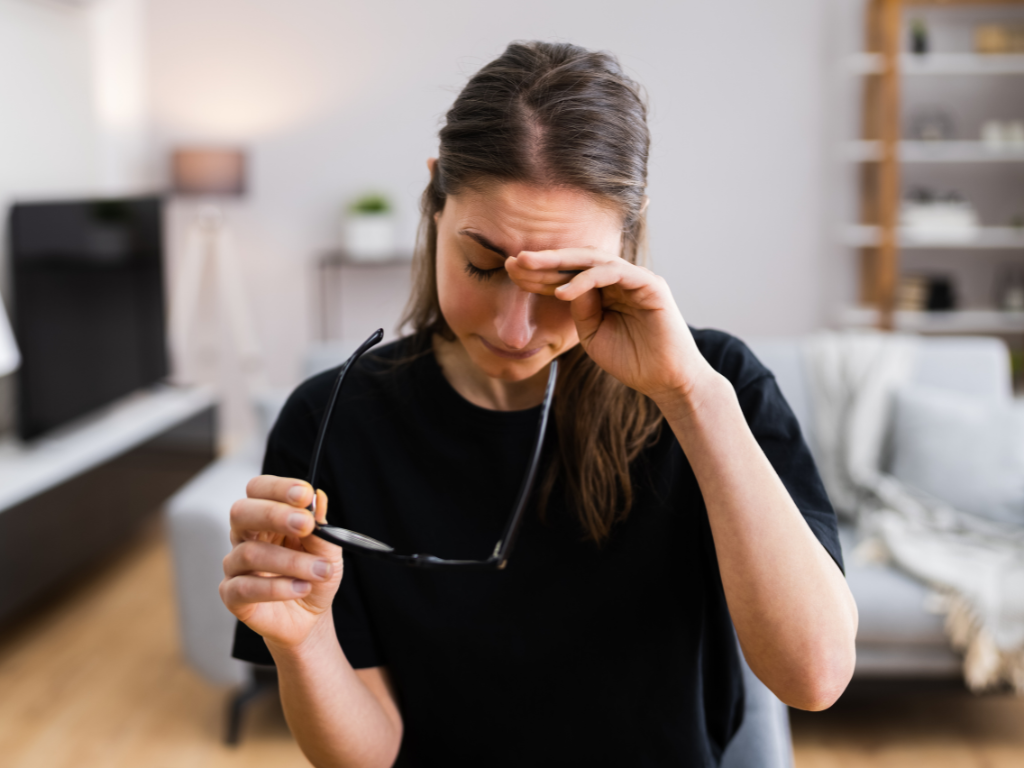 Woman rubbing her eye while holding her glasses in her hand